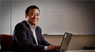 A seated smiling scientist on a laptop.