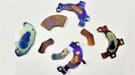 Four voice coil magnets taken from a desktop or laptop computer and their brackets (which have mounting holes).  These magnets are each about 10.5 – 15 grams, 1 - 1.25 inches long.  These ones are colorful, because they have been overheated in the process of separation and demagnetization. Photo supplied by the Ames Laboratory.