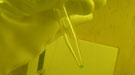 Scientist's gloved hand holding a small glass tube with a trace amount of green liquid 