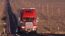 Tractor trailer driving down road flanked by fields