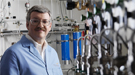 Scientist R. Morris Bullock standing in a laboratory with lab equipment in the background.
